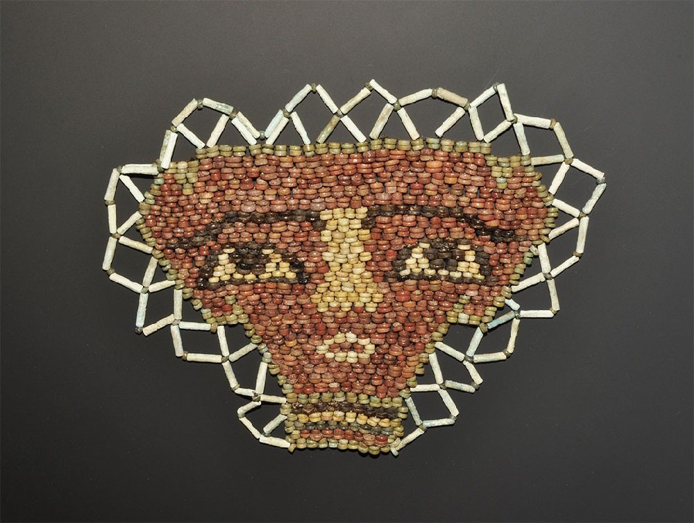 Egyptian Glazed Composition Mummy Bead Mask: Ptolemaic Period, 332-30 BC. A recently reconstructed beadwork face-mask of disc- and tubular-shaped glazed composition beads in red and other colours. 54 grams, 17.5cm (7"). Ex Paris collection and F