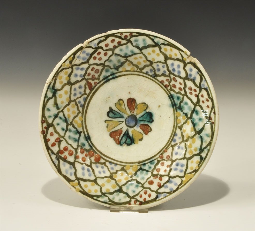 Islamic Glazed Ceramic Dish: An undated archaistic white-glazed dish with basal ring, central rosette in blue, red and yellow surrounded by a grid in green with pellet infill. 308 grams, 19cm (7 1/2"). Property of a London gentle
