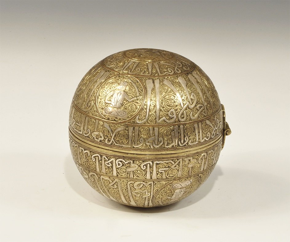 Islamic Bronze Hand-Warmer: An undated archaistic cast hand-warmer comprising two hinged hemispheres, silver-inlaid bands of arabesque ornament, roundels with silver-inlaid leaves between. 495 grams, 11.5 cm (4 1/2"). Property o