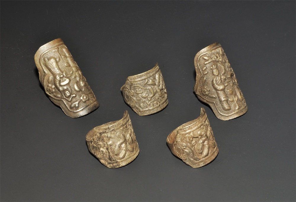 Chinese Silver Coloured Metal Repoussé Ring Group: 20th century AD. A mixed group of finger rings, each with narrow band and repoussé plaque with figural scene. 26 grams total, 22-39mm (3/4 - 1 1/2"). Property of a London gentleman; acquired before 1