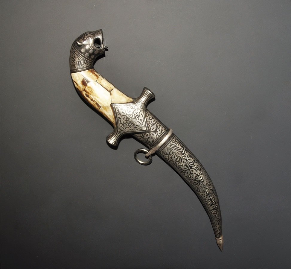 Islamic Ottoman Style Dagger: An undated archaistic steel-bladed dagger with curved hilt and lion-head pommel; bone panels to the grip; curved scabbard with chape and suspension ring. 219 grams, 26cm (10 1/4"). Acquired on the Lon
