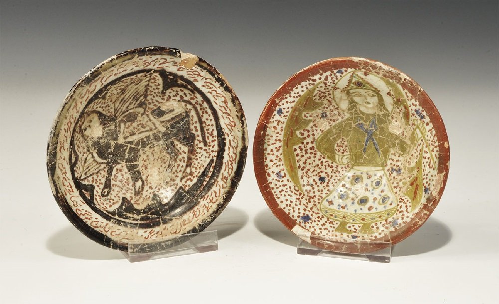 Islamic Glazed Ceramic Dish Pair: A group of two undated archaistic broad white-glazed dishes comprising: one with figure of a sphinx on a speckled field, band of red calligraphic text to the border; one with figure of a swordsman on 