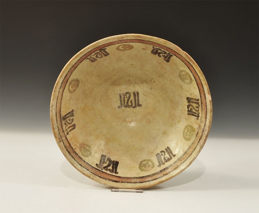 Islamic Glazed Ceramic Calligraphic Bowl: An undated archaistic glazed creamware conical bowl in12th century style with black-outlined red line beneath the rim, rosettes and blocks of calligraphic text below and additional text block to the c