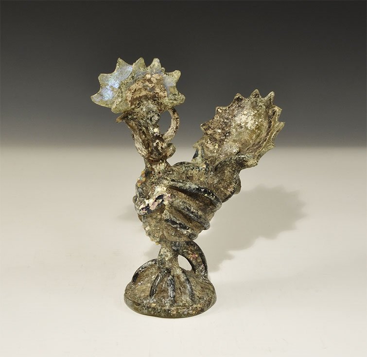 Islamic Glass Rooster Figurine: An undated archaistic cast iridescent glass figurine of a rooster in 12th century style on a domed base with scalloped tail. 670 grams, 21.5 cm (8 1/2"). From an old London collection, formed in the 1