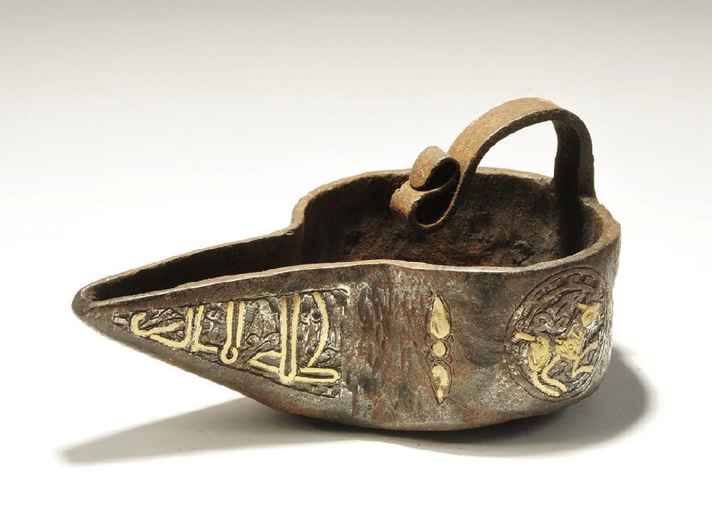 Islamic Iron Oil Lamp Filler with Gold and Silver Inlay: 18th century AD. A squat vessel with broad spout and recurved handle above; to the outer wall, a band of inlaid calligraphic text and sphinxes in roundels. 363 grams, 13.5cm (5 1/4"). Acquired on the