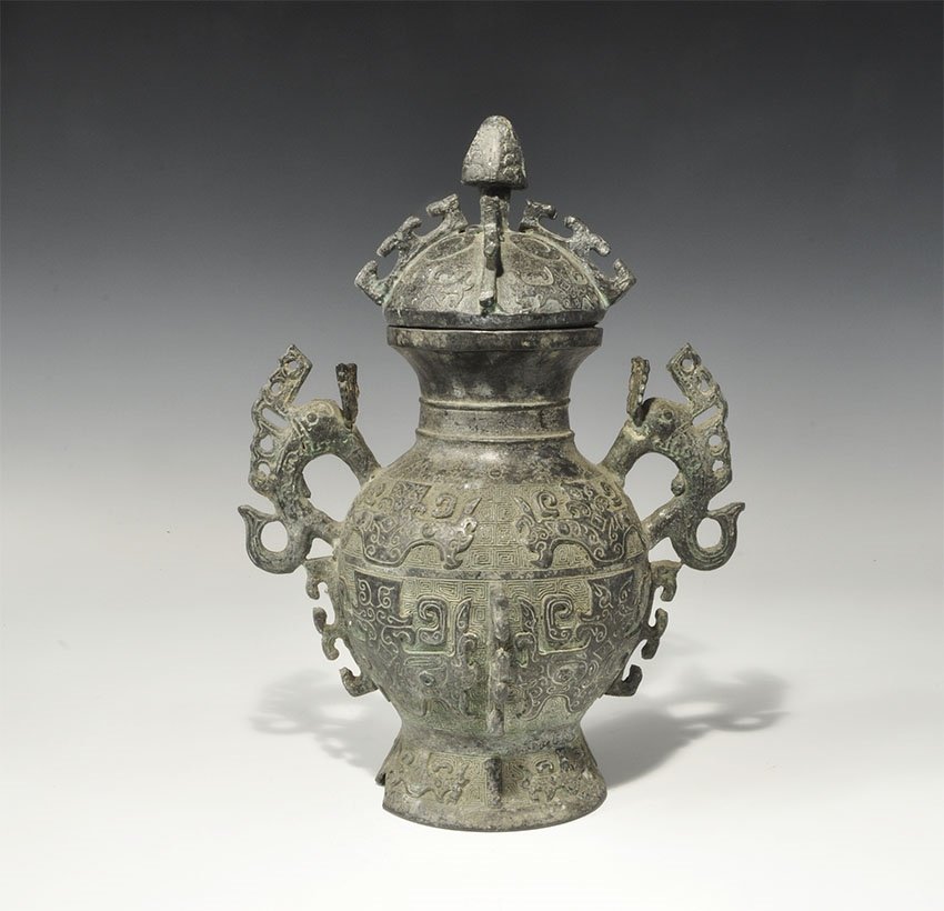Chinese Bronze Lidded Vessel: An undated archaistic hollow-cast Han Dynasty style vessel with bulbous body, flared base, waisted neck and domed lid; two fish-shaped handles and pierced scrolled flange to the body and lid; knop han