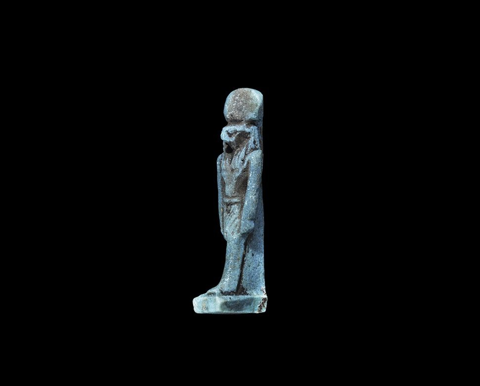 Egyptian Glazed Composition Horus Amulet: Saite Period, 624-525 BC. A deep blue amuletic pendant of falcon-headed Horus with dorsal pillar and rectangular base, wearing the double crown. See Andrews, C. Amulets of Ancient Egypt, London, 1994,