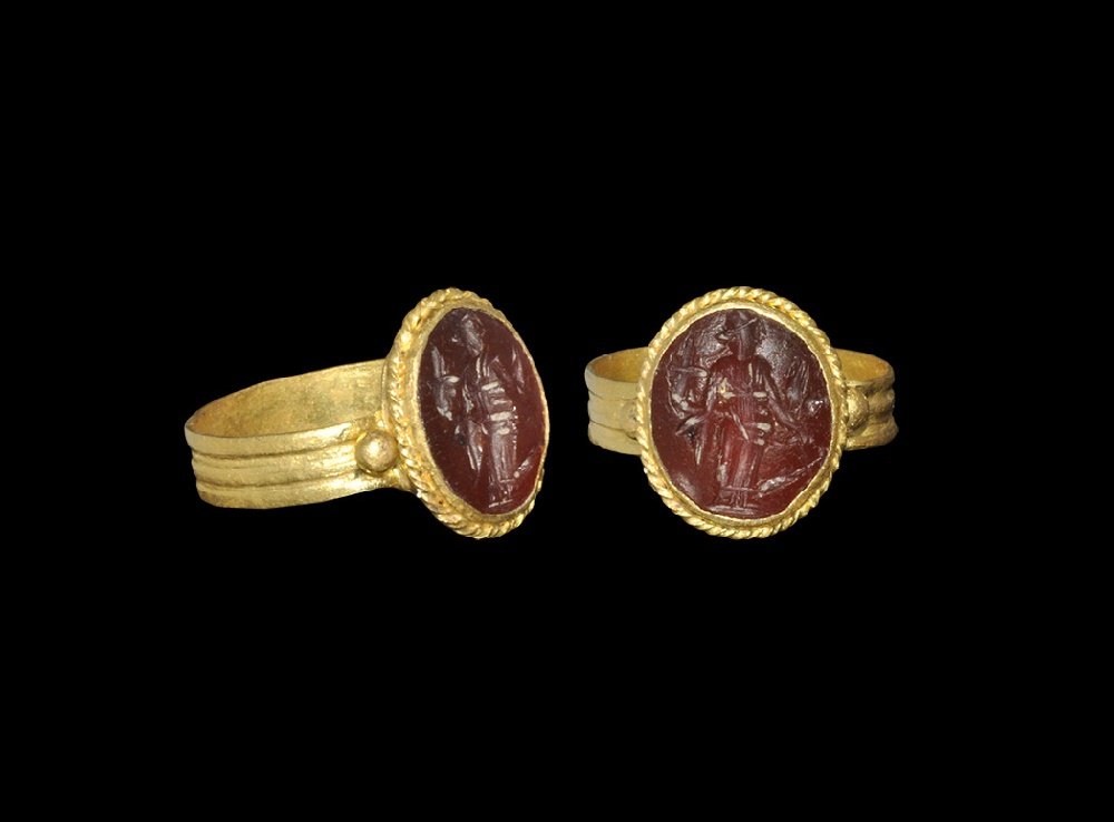 Roman Gold Ring with Fortuna Intaglio: 1st century BC-2nd century AD. A flat-section hoop with ribbed detailing, granules to the shoulders, discoid bezel with twisted filigree border, inset intaglio of Fortuna shown standing with cornucopi