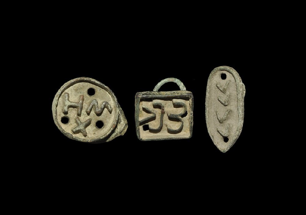 Byzantine Bronze Bread Stamp Group: 6th-12th century AD. A mixed group of cast bronze stamps, each with a suspension ring to the reverse, comprising: one round with 'HWX' and three holes; one shoe-shaped with '????' and two holes; one s