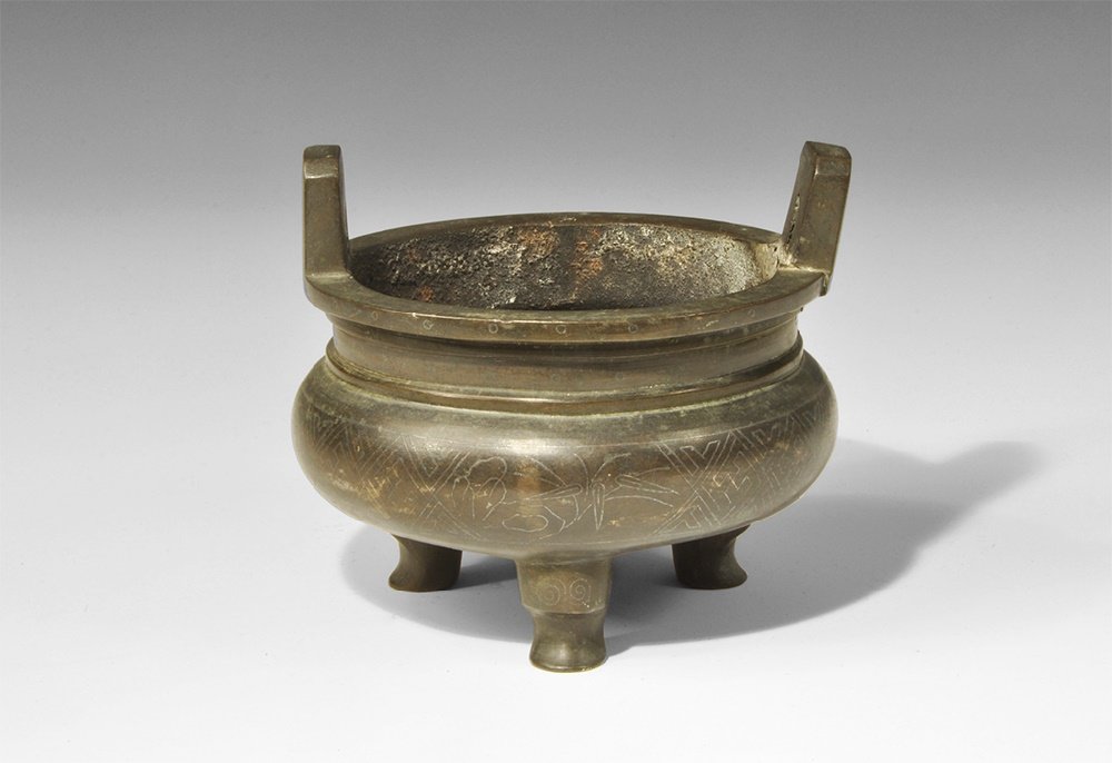 Chinese Bronze Incense Burner: Ming Dynasty, 1368-1644 AD. A cast bronze tripod pot with bulbous body and stepped shoulder, flat everted rim; to the legs, incised double-scroll motif; to the body geometric fret with foliate motifs 