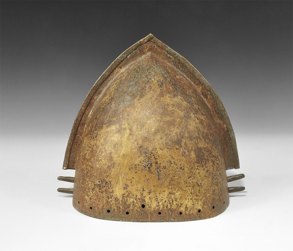 Bronze Age Vilanovan Crested Helmet: Circa 900 BC. A helmet made from two hammered bronze sheets, each with a flange to the upper edge and overlap at the flange and brim; the flanges beaten to form the crest, the brim overlap pierced fro