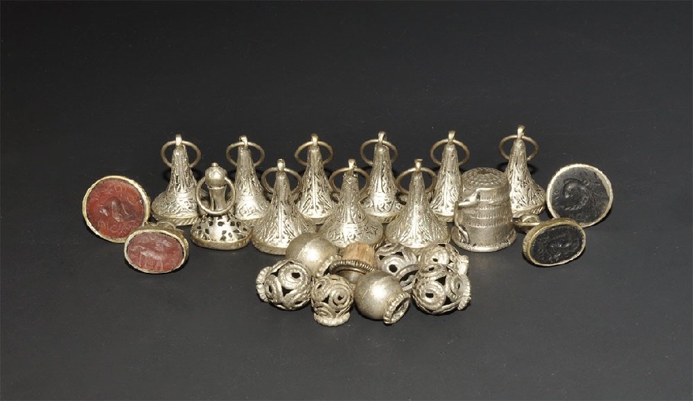 Near Eastern Seal and Bead Group: 20th century AD. A mixed group of twenty three silver-coloured metal discoid stamp seals with various stone intaglio to the base, white metal beads and a thimble. 111 grams total, 11-24mm (1/2 - 1").