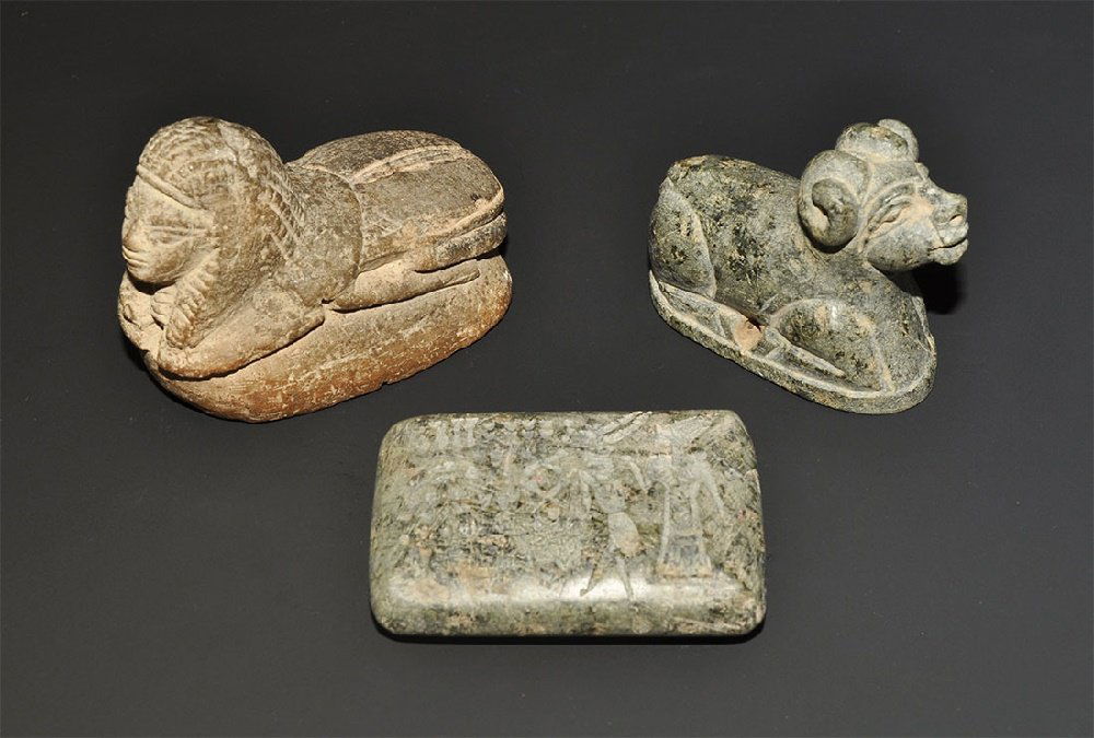 Egyptian Style Scaraboid and Tablet Group: A mixed group of undated archaistic items comprising: a green feldspar bifacial tablet with figures, a ram and Byblos script; a green feldspar seal matrix formed as a kneeling ram, figures and Ugariti