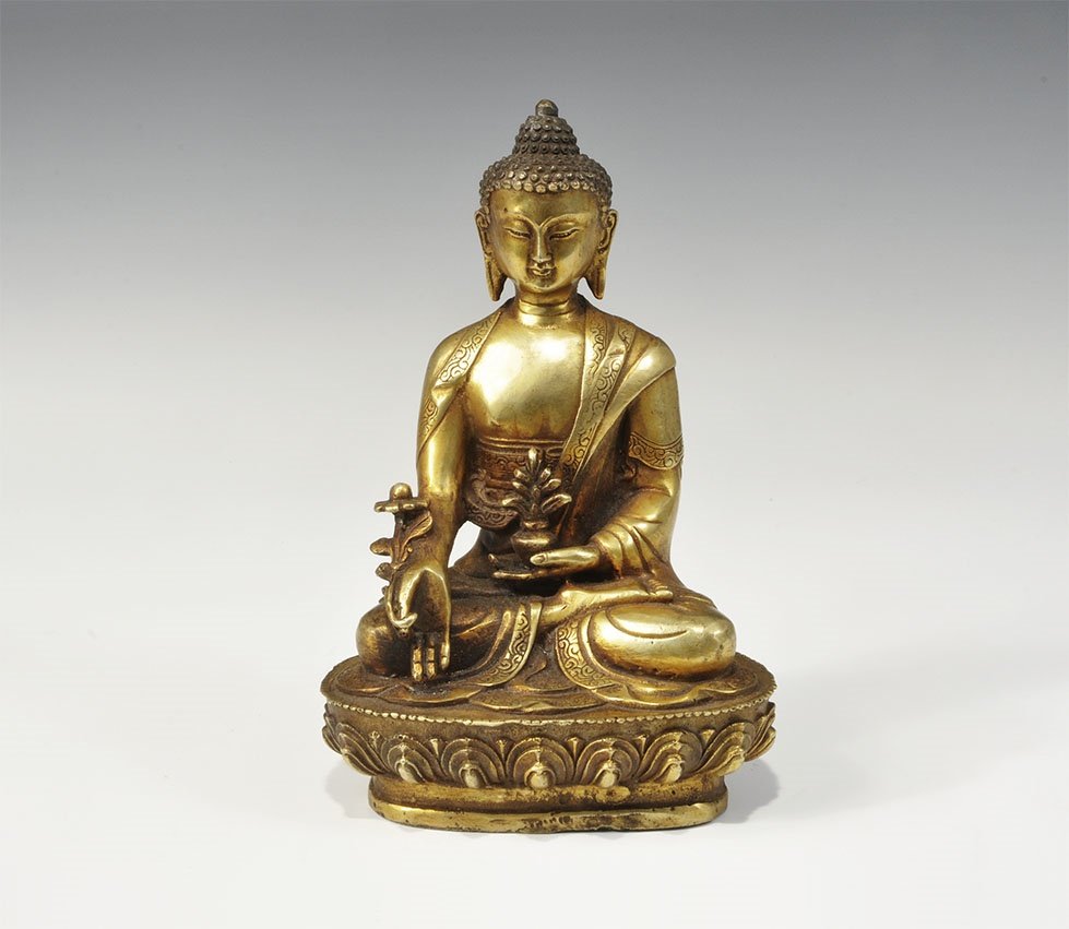Chinese Tibetan Style Gilt-Bronze Buddha Statuette: 20th century AD. A hollow-cast figure of Bhai?ajyaguruvai??ryaprabh?r?ja S?tra, the Medicine Buddha, seated cross-legged on a lotus flower base, flowers in the hands. 1.1 kg, 20cm (8"). Property of a