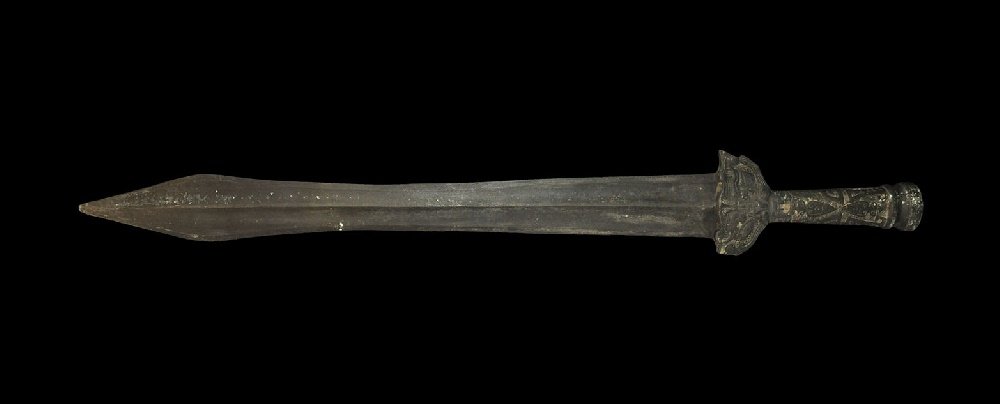 Chinese Style Bronze Sword: An undated archaistic Han Dynasty style sword with waisted blade, D-shaped lower guard and expanding grip; scrolled background and detail to the hilt, hollow pommel. 926 grams, 63cm (24 3/4"). From a 