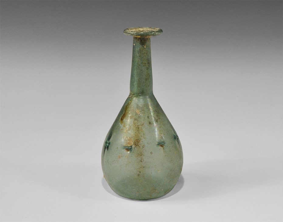 Roman Iridescent Blue Glass Pinched Bottle: 3rd-4th century AD. An iridescent blue bottle with dimple base, piriform body, tall neck and applied trail rim; to the shoulder, a series of pinched ledges. 68 grams, 15cm (6"). Property of a retired 