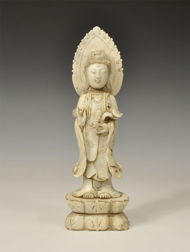 Chinese Style Serpentine Kwan Yin Statue: . An undated archaistic carved statuette of Kwan Yin standing with the right hand in the gesture of discussion, the left arm cradling a sceptre, nimbus to the rear of the head. 2.3 kg, 34.5 cm (13 3/4