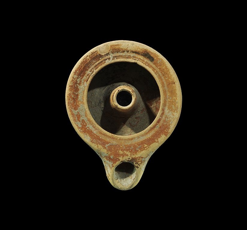 Greek Corinthian Terracotta Lamp: 5th century BC. A redware oil lamp with broad discus, D-shaped nozzle, central tubular projection into the oil chamber. 142 grams, 11.5cm (4 1/2"). Acquired on the London art market prior to 1980.
