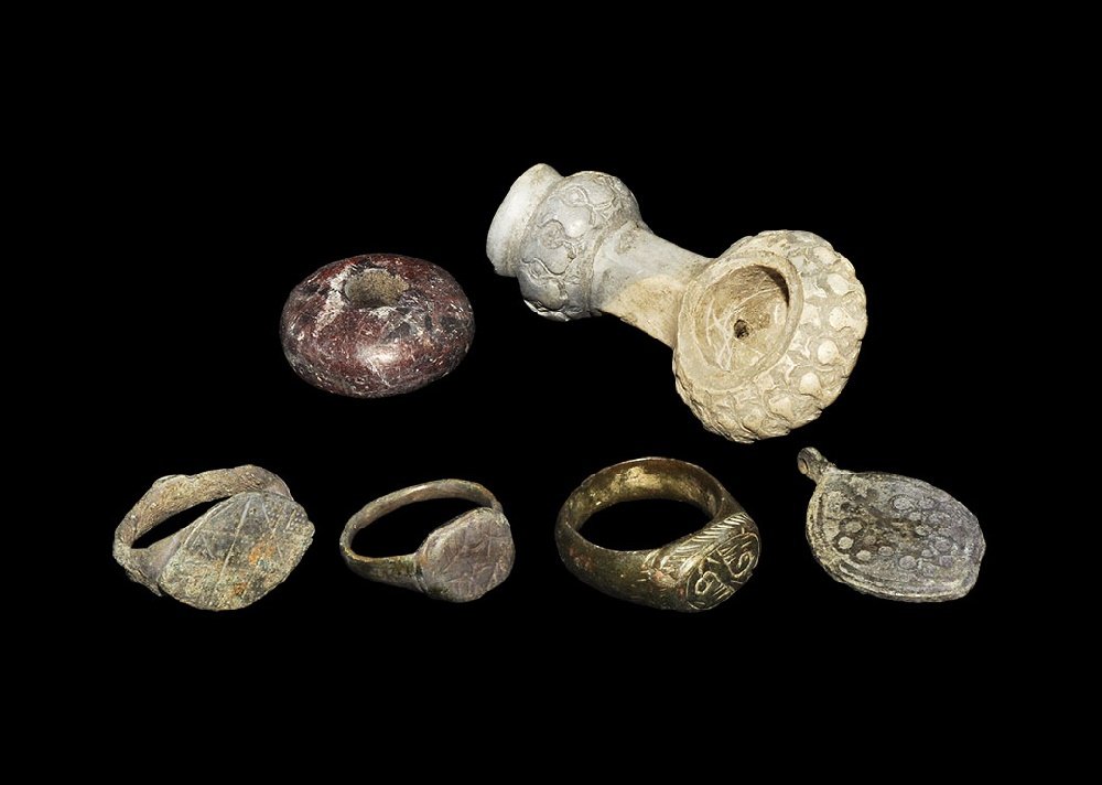 Byzantine Bronze Ring and Other Items Group: 6th-12th century AD. A mixed group of items comprising: a steatite (?) pipe bowl; a red hardstone spindle whorl; a bronze mandorla pendant with bunch-of-grapes motif to each face; three bronze finger
