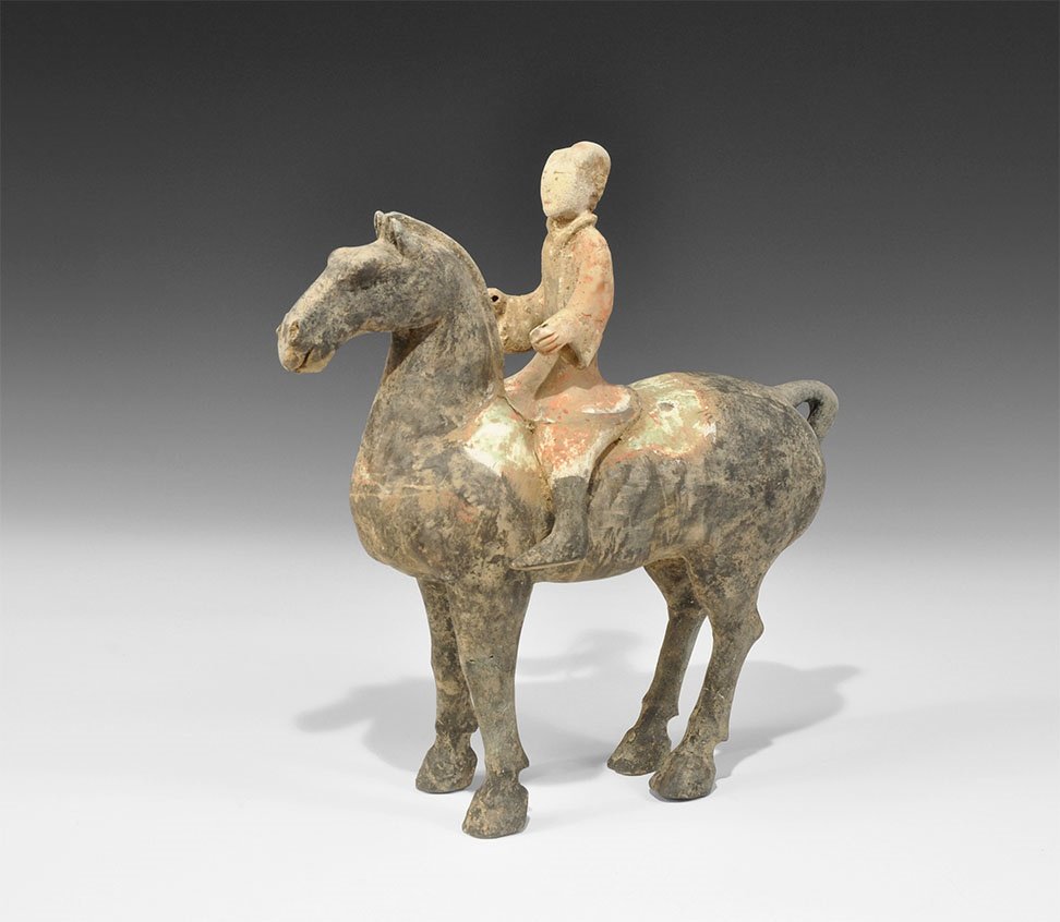 Chinese Ceramic Horse and Rider Figurine: Han Dynasty, 206 BC-220 AD. A hollow-formed horse in standing pose with arched neck and looped tail, rider in short coat with wide sleeves; the horse and rider's boots painted black, the saddle in whi