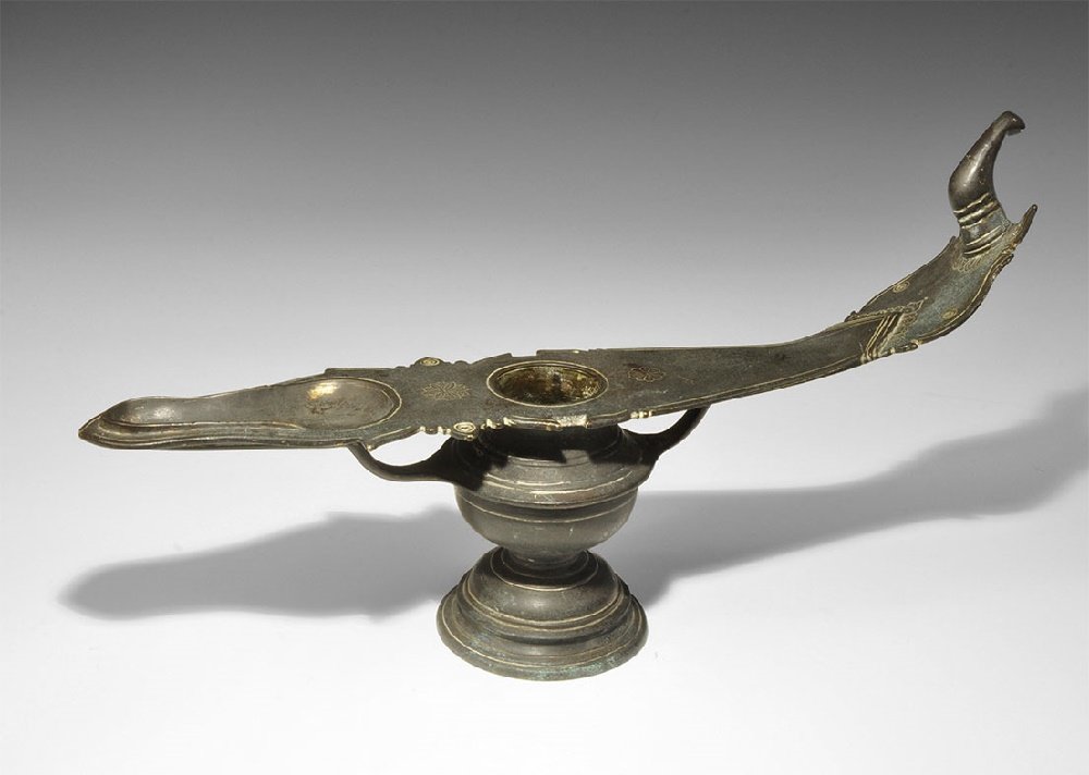 Indian Bronze Oil Lamp: 19th century AD. A pedestal base and drum-shaped body with flared rim and two curved arms supporting a broad plaque with shallow piriform recess, curved end with hook; incised rosette and floral detai