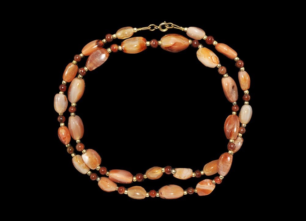 Vintage Carnelian Bead Necklace: 20th century AD. A necklace of graduated triangular-section rounded carnelian beads from India with interstitial small globular beads and gilt metal spacer beads. 75 grams, 74cm (29"). Private collect
