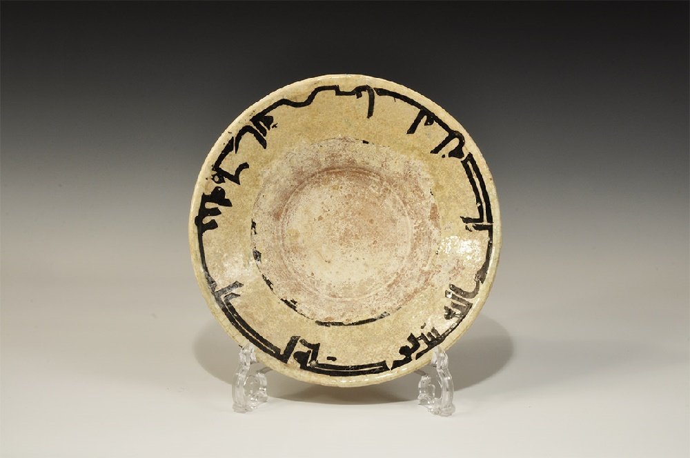 Islamic Style Glazed Ceramic Bowl: A broad, shallow funicular undated archaistic bowl with basal ring, buff-glazed with band of Kufic text to the inner face. 732 grams, 25.5cm (10"). Property of a London gentleman; acquired before 1996