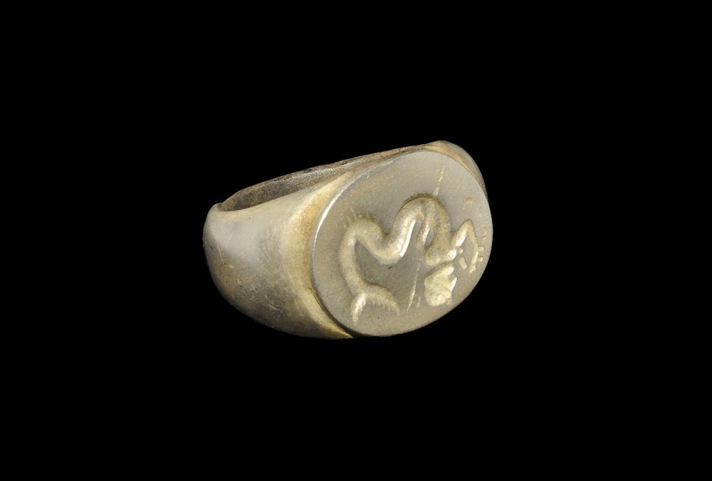Roman Style Silver-Gilt Triton Ring: 20th century AD. A broad D-section hoop with expanding shoulders, discoid plaque with intaglio image of Triton with a spear. 24 grams, 29mm overall, 20.49mm internal diameter (approximate size British