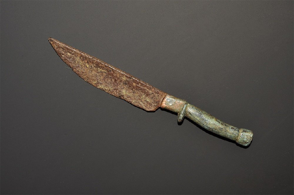Roman Style Bronze-Handled Knife: A small undated archaistic knife with single-edged curved blade, square-section bolster with spur to the underside, round-section handle with knop finial. 70 grams, 16cm (6 1/4"). Private collection, 