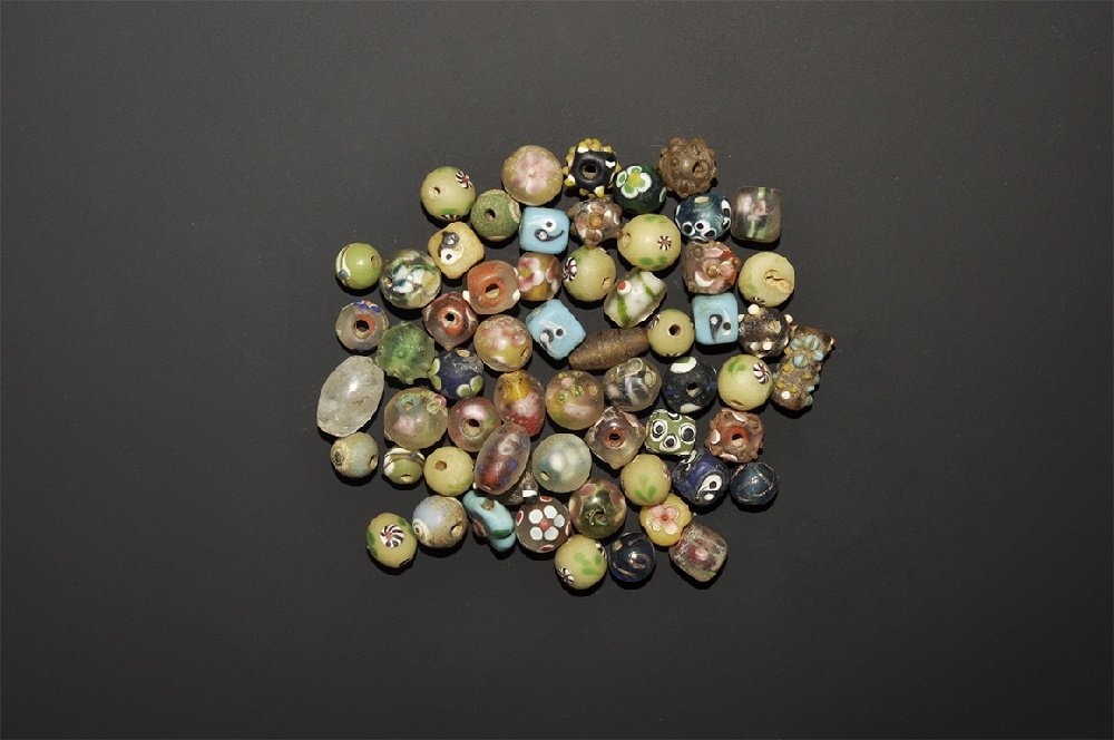 Islamic Safavid Style Glass Bead Collection: 20th century AD. A mixed group of beads comprising: seven cuboid; six cuboid with applied knops; six globular with applied knops; thirty three globular; nine irregular. 128 grams total, 9-17mm (1/4 - 