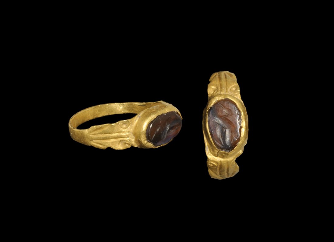 Roman Gold and Garnet Decorated Ring with Crane: 3rd century AD. A flat-section hoop with flared shoulders, volute scrolls; discoid plaque with inset garnet intaglio of a crane. 1.76 grams, 17mm overall, 15.77mm internal diameter (approximate size B