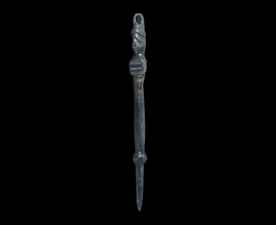 Roman Bronze Stylus Pendant with Face: 1st-3rd century AD. A round-section tapering shank with bulb above the tip, rectangular block with transverse slits, helmetted head of Minerva(?) with crest forming the suspension loop. 18 grams, 98mm