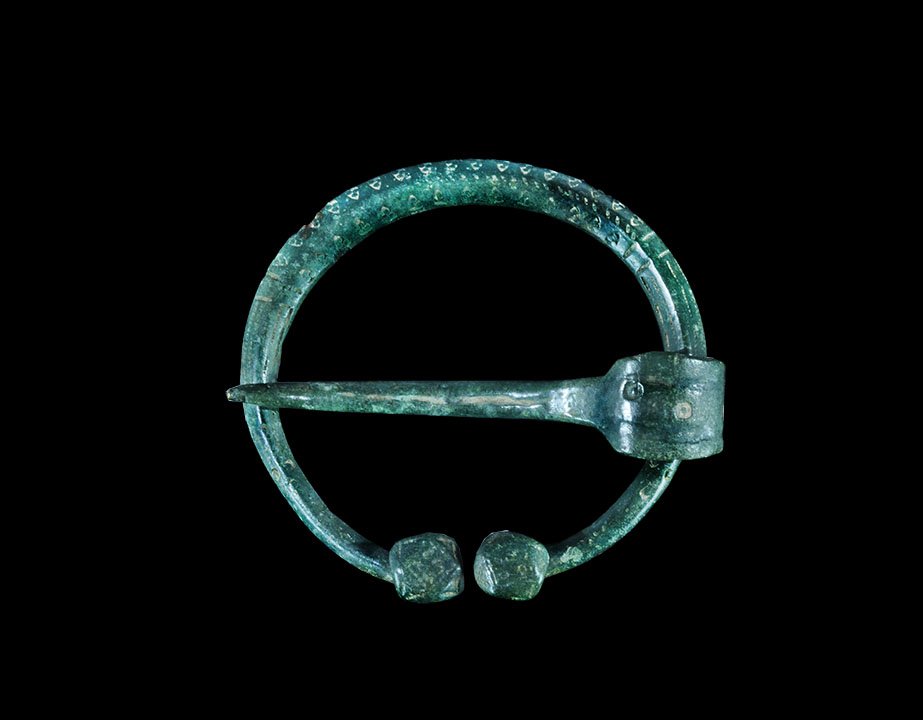 Viking Bronze Penannular Brooch: 9th-12th century AD. A lozenge-section penannular shank with perpendicular facetted square terminals; two bands of punched triangles to the upper face, each with a dot to each angle; pellets to the te