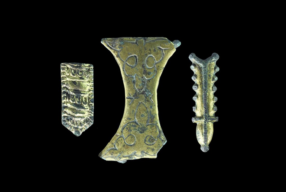 Viking Gilt-Bronze Belt Mount Group: 8th-12th century AD. A mixed group comprising: a waisted plaque with incised loop detail, pins to the reverse; a D-section bar with bulb finial, linear rib to the upper face, knops to the sides; a ton