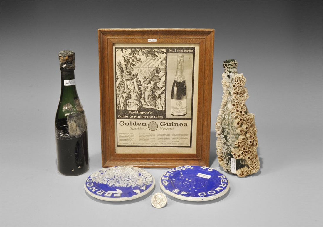 Shipwreck Muscatel Bottles and Pernod Ashtray Group: 20th century AD. A mixed group of finds recovered from the wreck of the MV Seine comprising: a green glass dimple-bottomed bottle of 'Golden Guinea' muscatel wine, corked and with most of the contents