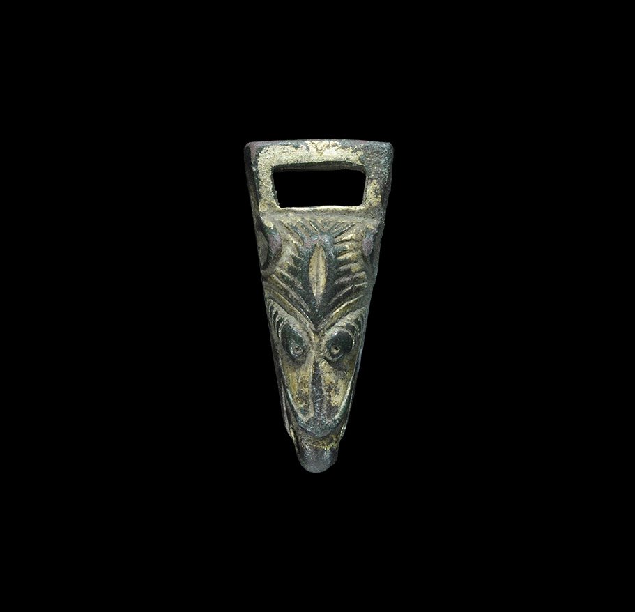 Anglo-Saxon Gilt-Bronze Wolf's Head Strap End: 8th-9th century AD. A cast strap fitting comprising a trapezoidal plaque with rectangular slot at the broad end; the outer face with a stylised wolf's head modelled in the half-round, the jaws open wi