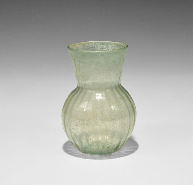 Anglo-Saxon Green Glass Pouch Bottle: 5th-6th century AD. A pale green pouch bottle with bulbous body and funicular neck, indented base; the body and neck with vertical ribbing. 70 grams, 11.5 cm (4 1/2"). From an important Dutch collecti