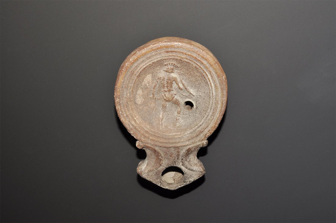 Roman Oil Lamp with Gladiator: . An undated archaistic oil lamp in 1st century AD style, a broad discus and broad nozzle with volute scrolls to the neck, low-relief figure of a gladiator seen from the rear. 75 grams, 98mm (4"). Pro