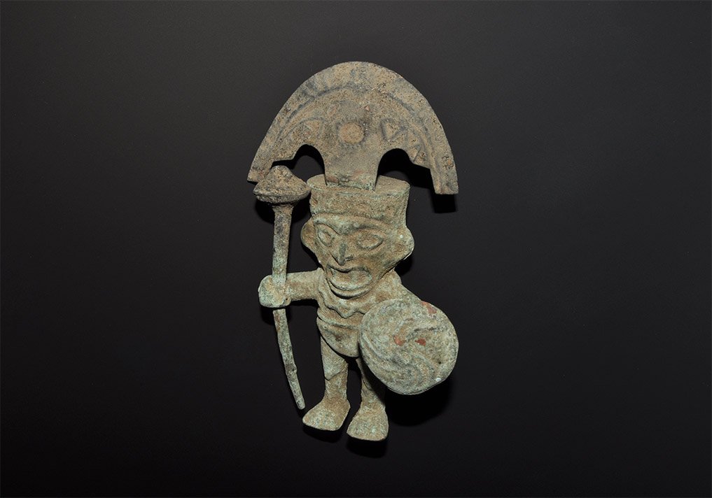 Pre-Columbian Peruvian Moche Style Bronze Warrior: . A hollow-formed undated archaistic figurine of a warrior modelled in the round, clutching a mace and shield, with the broad headdress of a distinguished personage, 97 grams, 17cm (6 3/4"). From an o