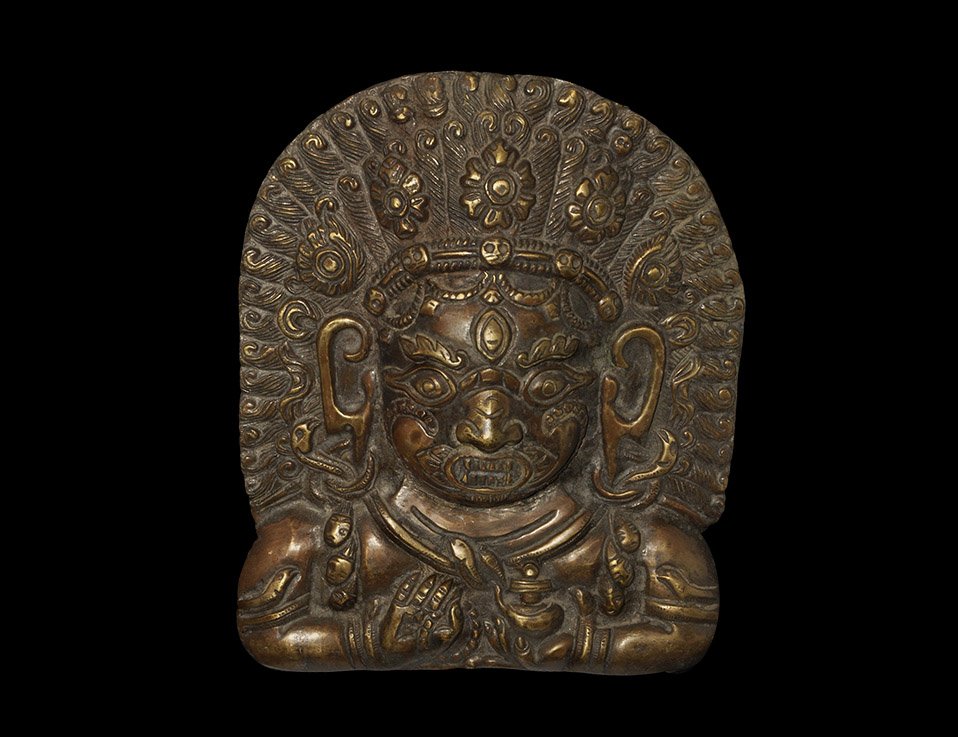 Indian Nepalese Bronze Bhairava Head Applique: Nepal, 19h-early 20th century AD. Cast bronze applique head of the Hindu god Bhaiarva shown with a grimacing leonine face with hair arranged in a tall frame around the head supported by a diadem with 
