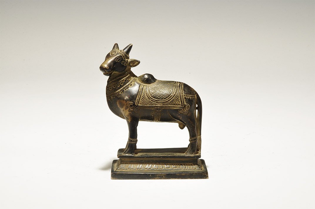 Indian Bronze Ox Statuette: India, 19th-early 20th century AD. A hollow-case model ox with harness and decorative coverings standing on a pedestal base. 496 grams, 11.5cm (4 1/2"). Property of a London gentleman; acquired before
