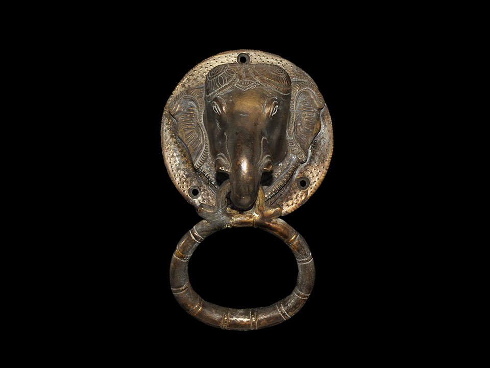 Indian Bronze Elephant-Head Door Handle: India, 19th-early 20th century AD. A cast convex discoid plaque with elephant's head modelled in the round; trunk looped to hold a bamboo-effect ring; plaque with three holes for attachment. 1.1 kg, 1