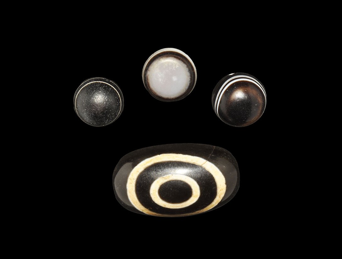 Chinese Tibetan Style Eye Bead Group: A mixed group of undated archaistic black glass eye beads, three circular in plan and one ovoid. known as Dzi these beads are worn as either necklaces or bracelets and are believed to have protective 