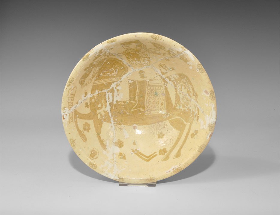 Islamic Glazed Figural Bowl: An undated archaistic buff-glazed ceramic bowl with ochre design of a horseman with a bird on his left wrist, foliage in the field. 564 grams, 22.5cm (9"). Acquired on the London art market before 199
