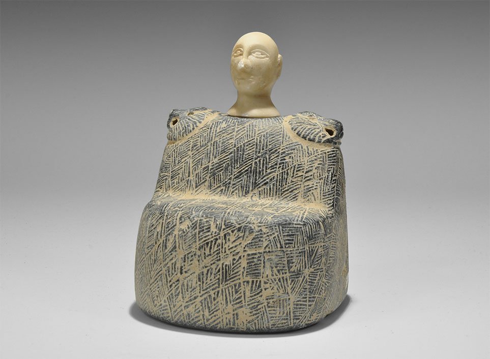 Western Asiatic 'Bactrian' Idol with Head: An undated archaistic carved steatite idol of a seated figure in a hatched cloak with pierced beast-head shoulder panels; separate carved white stone head. 2 kg, 14.5cm (5 3/4"). UK art market, acquir