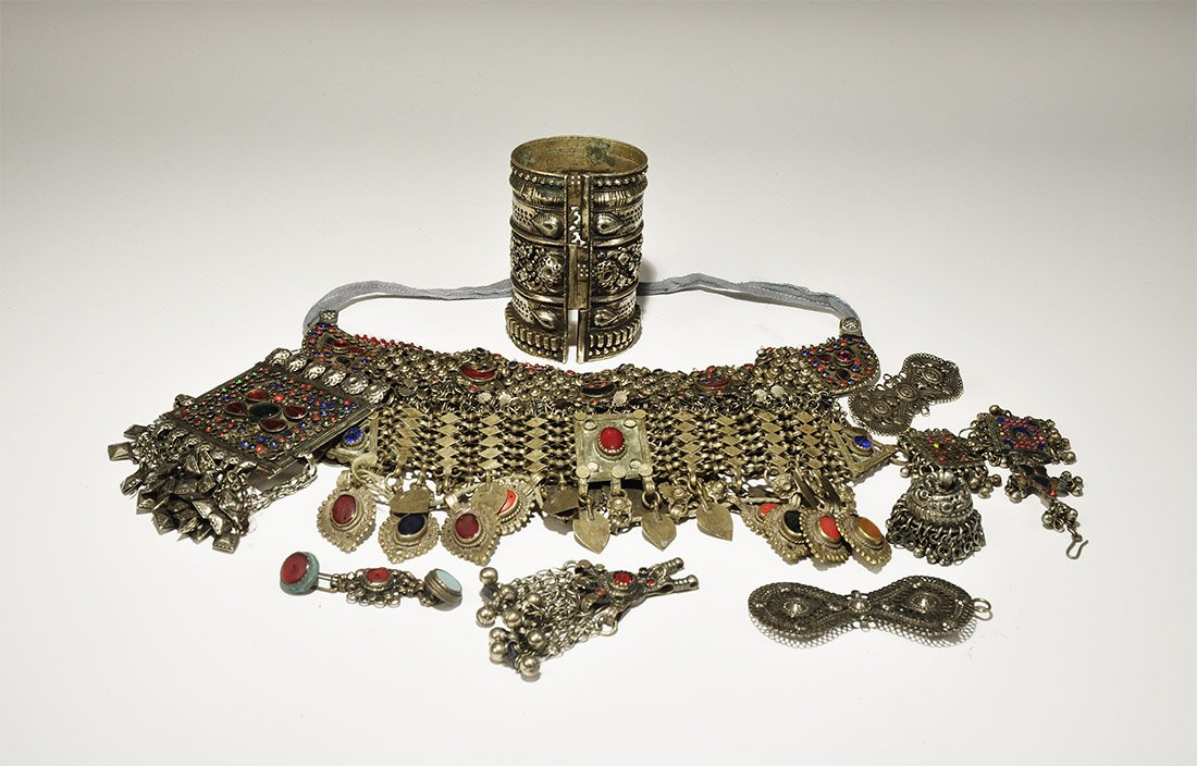 Ethnographic Bedouin Jewellery Group: 20th century AD. A mixed group comprising: a fabric-backed choker with coin dangles; an articulated choker with glass inserts and dangles; a button-clasp with glass inserts; five pendants with dangles