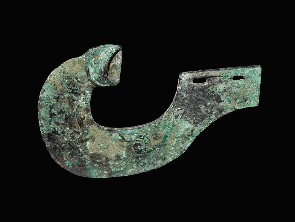 Chinese Decorated Halberd: Zhou Dynasty 1046-256 BC. A bronze halberd blade, C-shaped in plan, decorated with serpentine patterning in low relief; tang and animal-head socket pierced for attachment. 570 grams, 20cm (8"). Privat