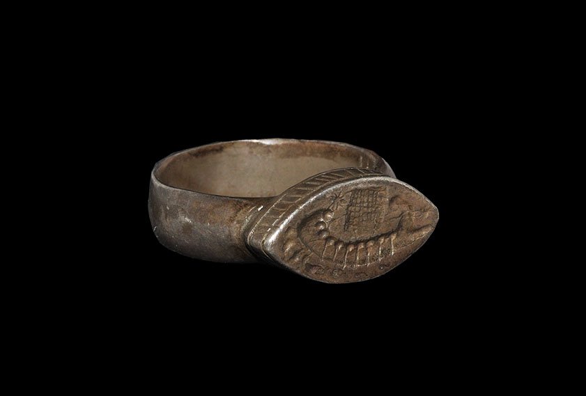 Roman Style Galley Signet Ring: 20th century AD. A flat-section pewter (?) hoop rising to carinated shoulders, scaphoid bezel with ropework sidewall, intaglio motif of a trireme under sail, stars and foliage in the field. 9.42 grams