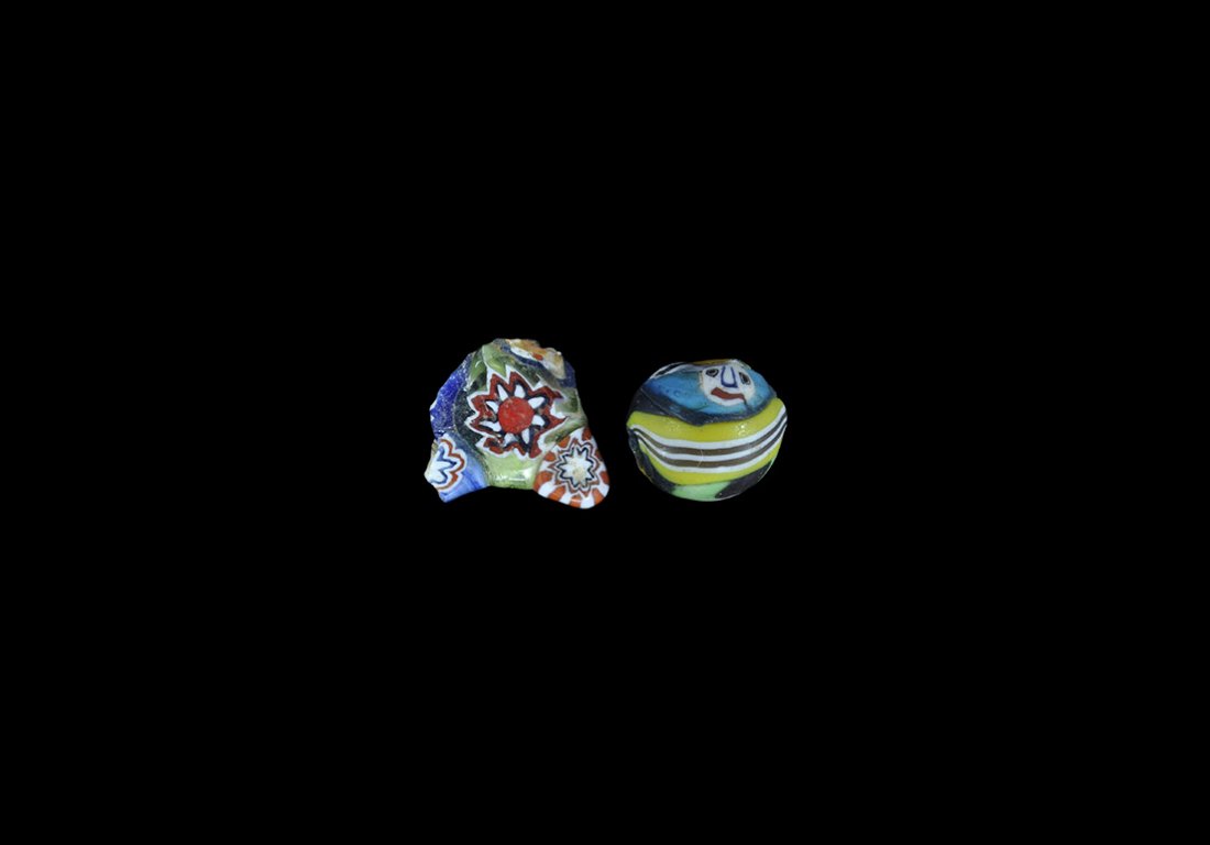 Islamic Face Bead and Floral Fragment: 19th-20th century AD. A mixed group comprising: a globular mosaic glass bead with two faces; a discoid glass bead fragment with knops to the edge, floral detailing. 5.03 grams, 13-15mm (1/2"). From an