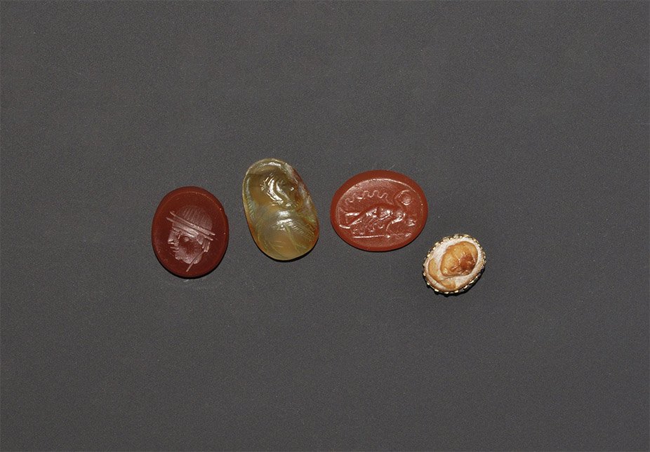 Post Medieval Carnelian Intaglio and Cameo Group: 17th century AD and later. A mixed group of Roman design carnelian intaglios and a cameo comprising: a profile male bust with sallet; a female dancer, nude with flower, platter and streamers; a profil